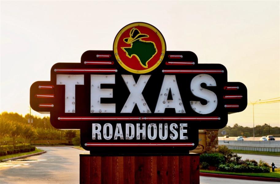 Texas Roadhouse restaurant sign on the side of a freeway in Humble, Texas during an early morning sunrise.